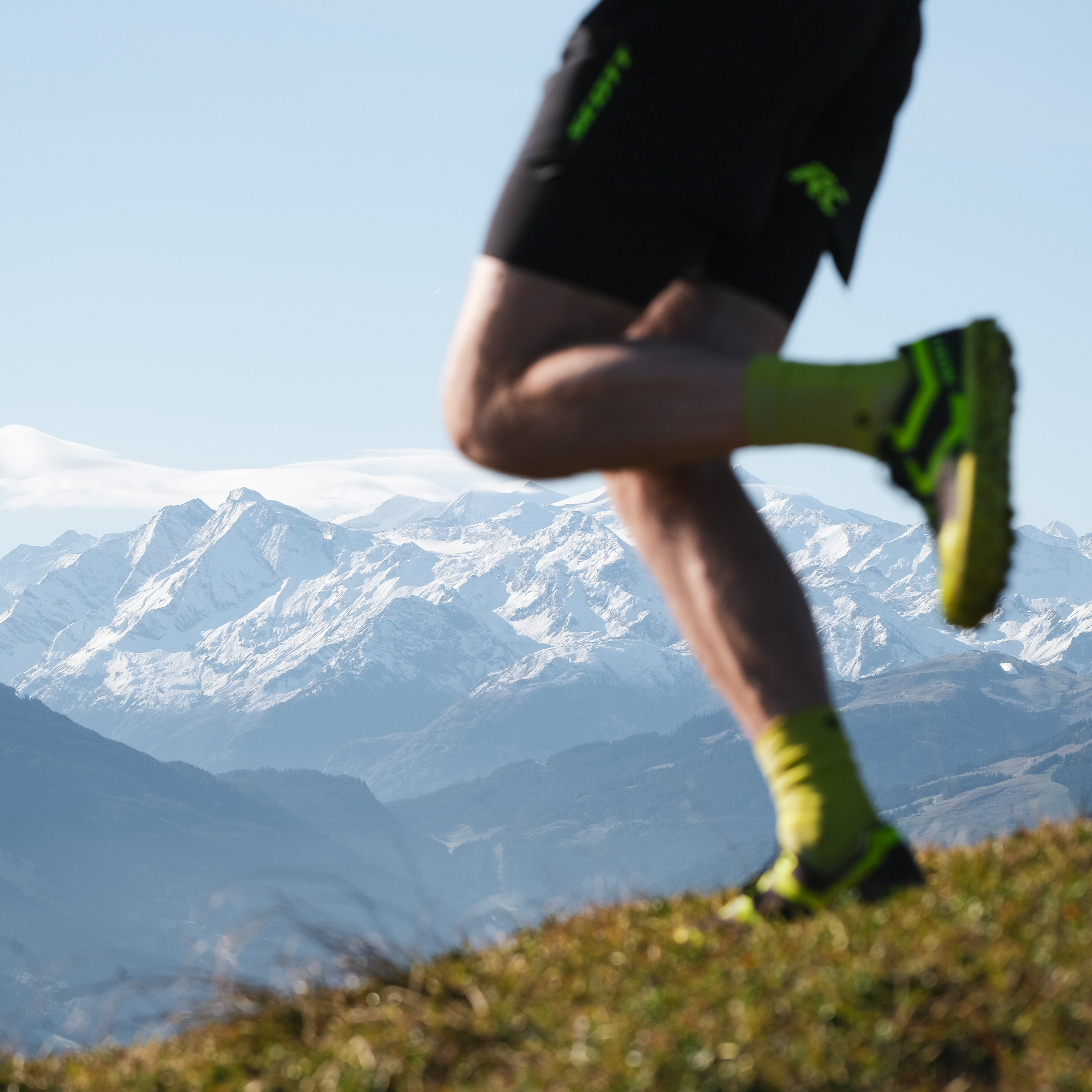 On Tour Paul Doyle Trailrunning Kitzbüheler Horn Herbst (c) Kitzbühel Tourismus Der Fokus liegt auf dem Bein eines Sportlers, der in den Alpen joggt, während majestätische Berge die Landschaft prägen.