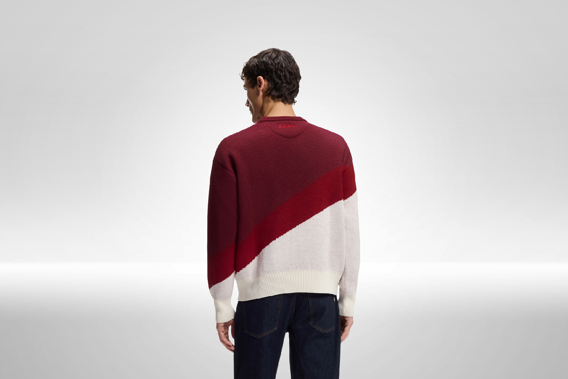 Ein Mann trägt einen modischen Pullover mit diagonalen Farbstreifen in Rot und Weiß, während er in die Kamera schaut.