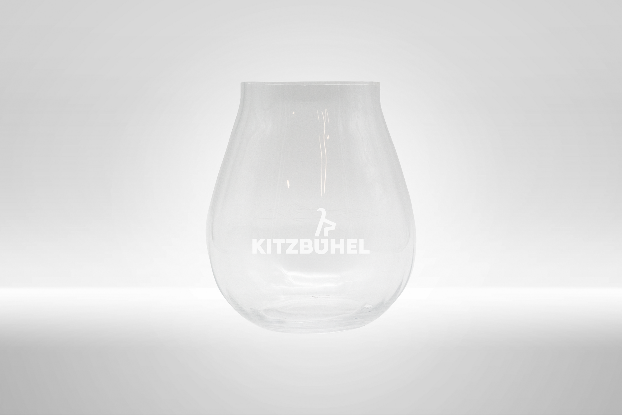 Ein elegantes, transparentes Glas mit dem Schriftzug 'KITZBÜHEL' auf der Vorderseite, vor einem hellen Hintergrund.