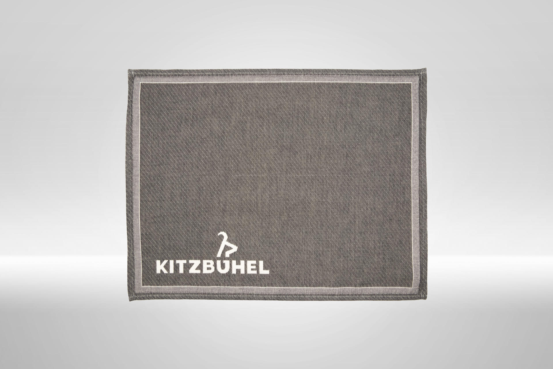 Ein graues Platzset mit einem weißen Rand und dem Schriftzug 'KITZBÜHEL' in der unteren rechten Ecke.