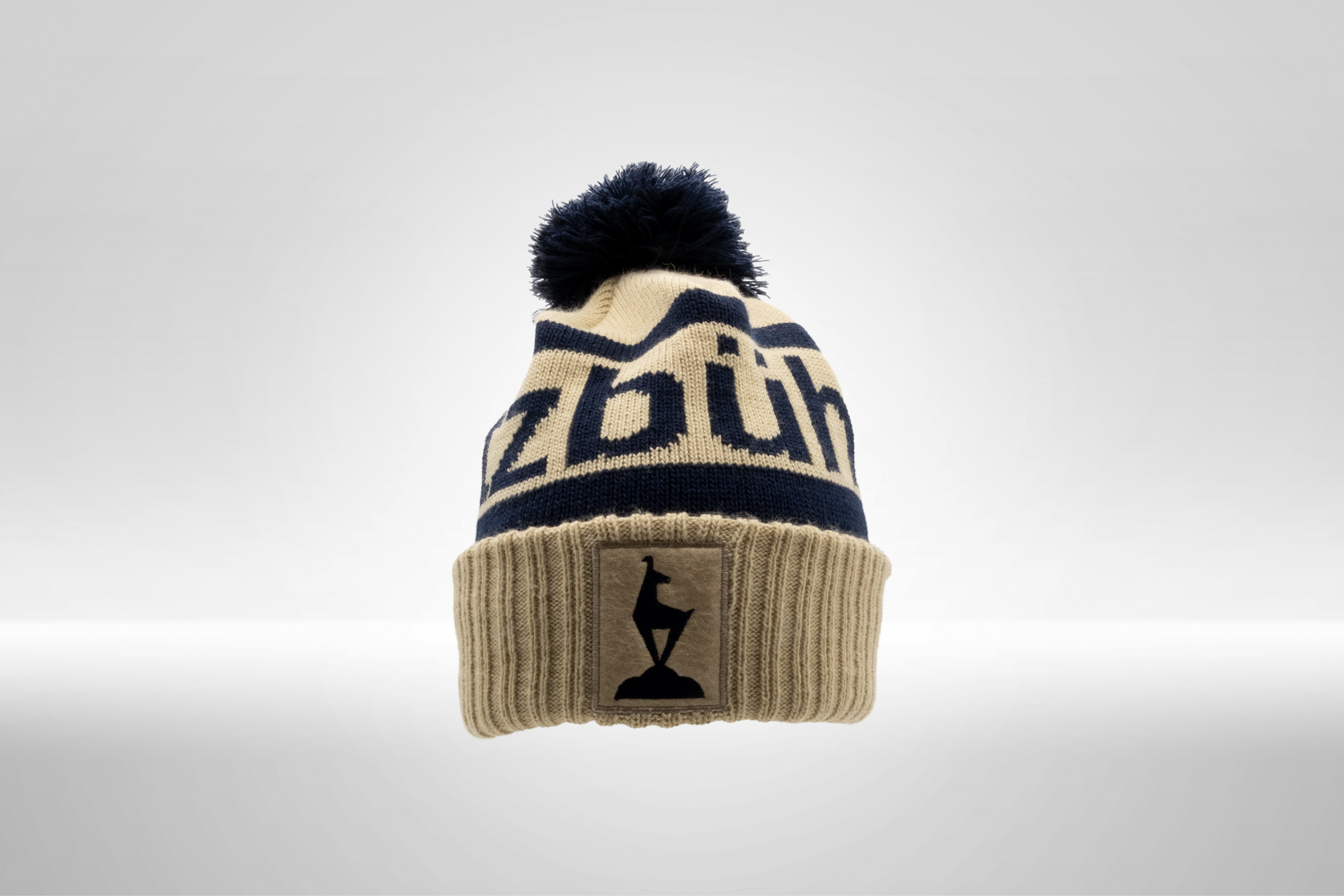 Eine beige Strickmütze mit blauen Akzenten und einem großen Pompon auf der Oberseite, ideal für kalte Tage.