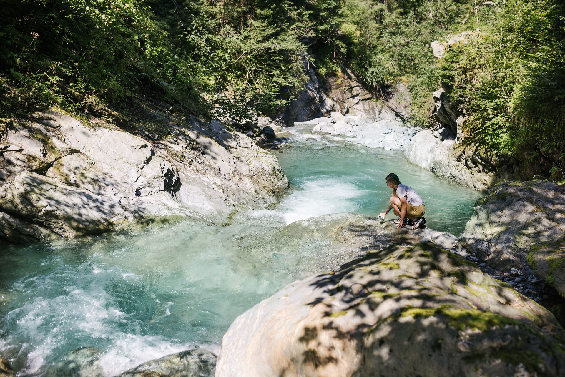 Person, die auf einem Felsen sitzt und aufs Wasser schaut